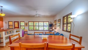A dining area with a wooden table and chairs, a ceiling fan, and large windows with blinds. - Bright and airy beachfront villa located in Soliman Bay with a New Pool (Tulum)