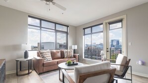 Un salón amplio con un gran ventanal, un ventilador de techo y vistas a la silueta de la ciudad.