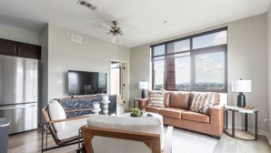 Una sala de estar moderna con un sofá, una silla, un televisor, una zona de comedor con mesa y un ventanal con vistas.