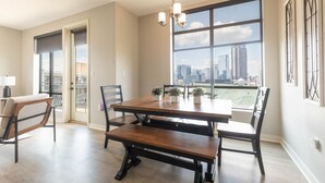 Un comedor con una mesa grande, sillas, una araña y vistas a la ciudad a través de amplios ventanales.