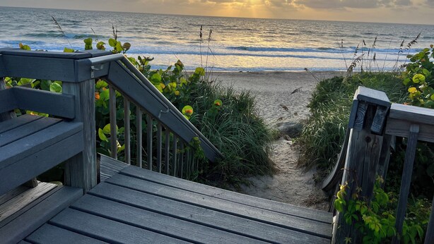 A wooden staircase leading to a beach with a view of the ocean and a sunset. - Beachfront! 3rd Floor Corner Unit, Enjoy Sunrise to Sunset (Stuart)