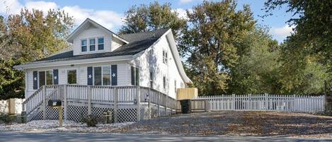 A two-story house with a white exterior, a porch with a wooden railing, and a white picket fence.