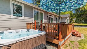 A hot tub in front of a house with a wooden deck and a patio umbrella. - Gorgeous, Spacious and Well Lit Hot Tub Home with Large Deck for Entertaining. (Rockaway Beach)