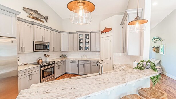 A modern kitchen with white cabinets, a large island, stainless steel appliances, and wooden stools. - Gorgeous, Spacious and Well Lit Hot Tub Home with Large Deck for Entertaining. (Rockaway Beach)