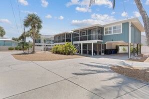 A modern two-story building with a covered outdoor seating area and a covered garage. - Beach Bungalow 1....Perfect duplex with shared pool (Fort Myers Beach)
