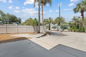 A paved outdoor area with palm trees, a white fence, and a clear sky. - Beach Bungalow 1....Perfect duplex with shared pool (Fort Myers Beach)