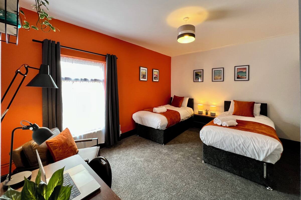 A hotel room with two beds, a desk with a laptop, a desk lamp, and a potted plant.