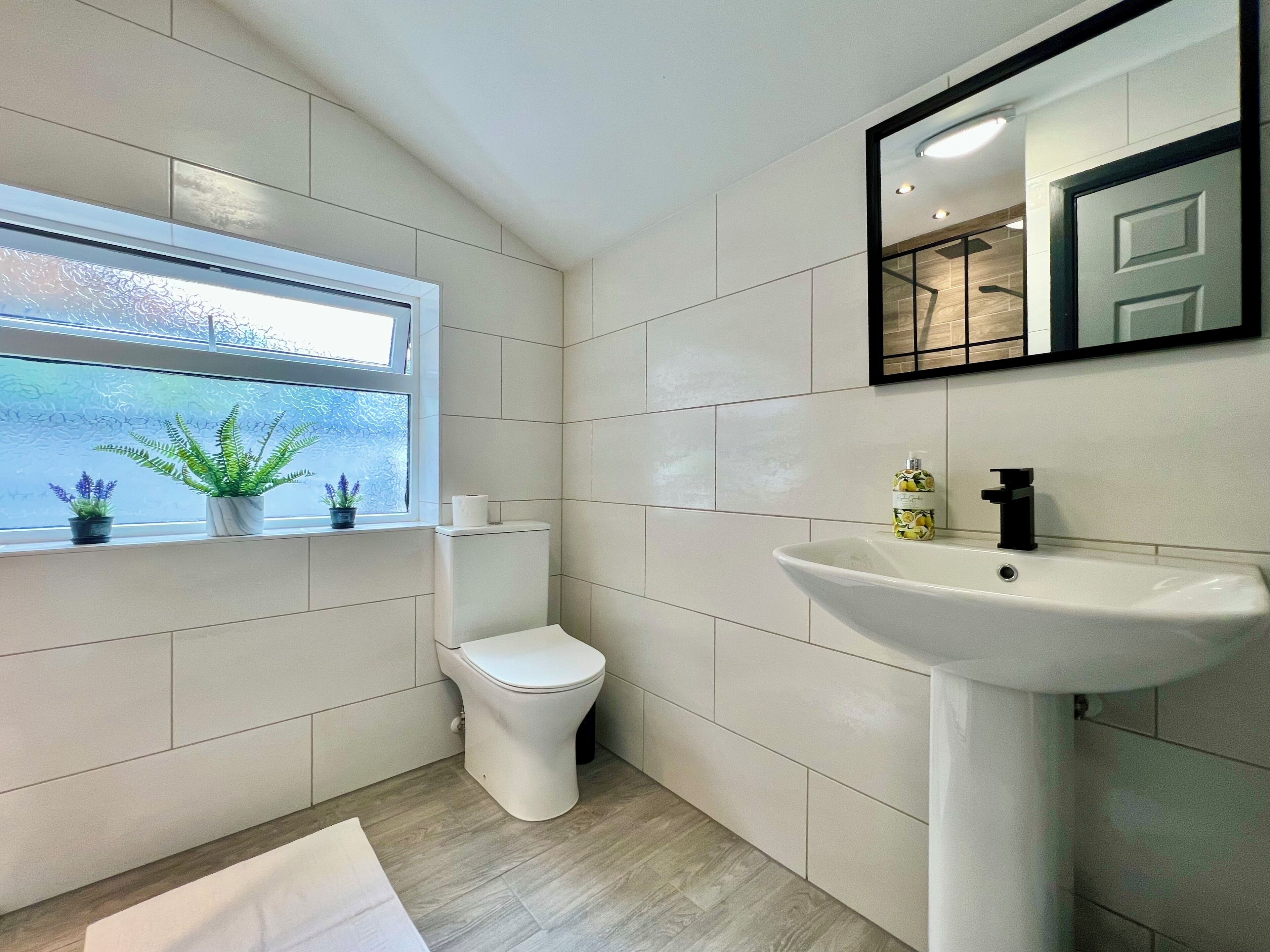 A modern bathroom with a toilet, sink, and window with plants.