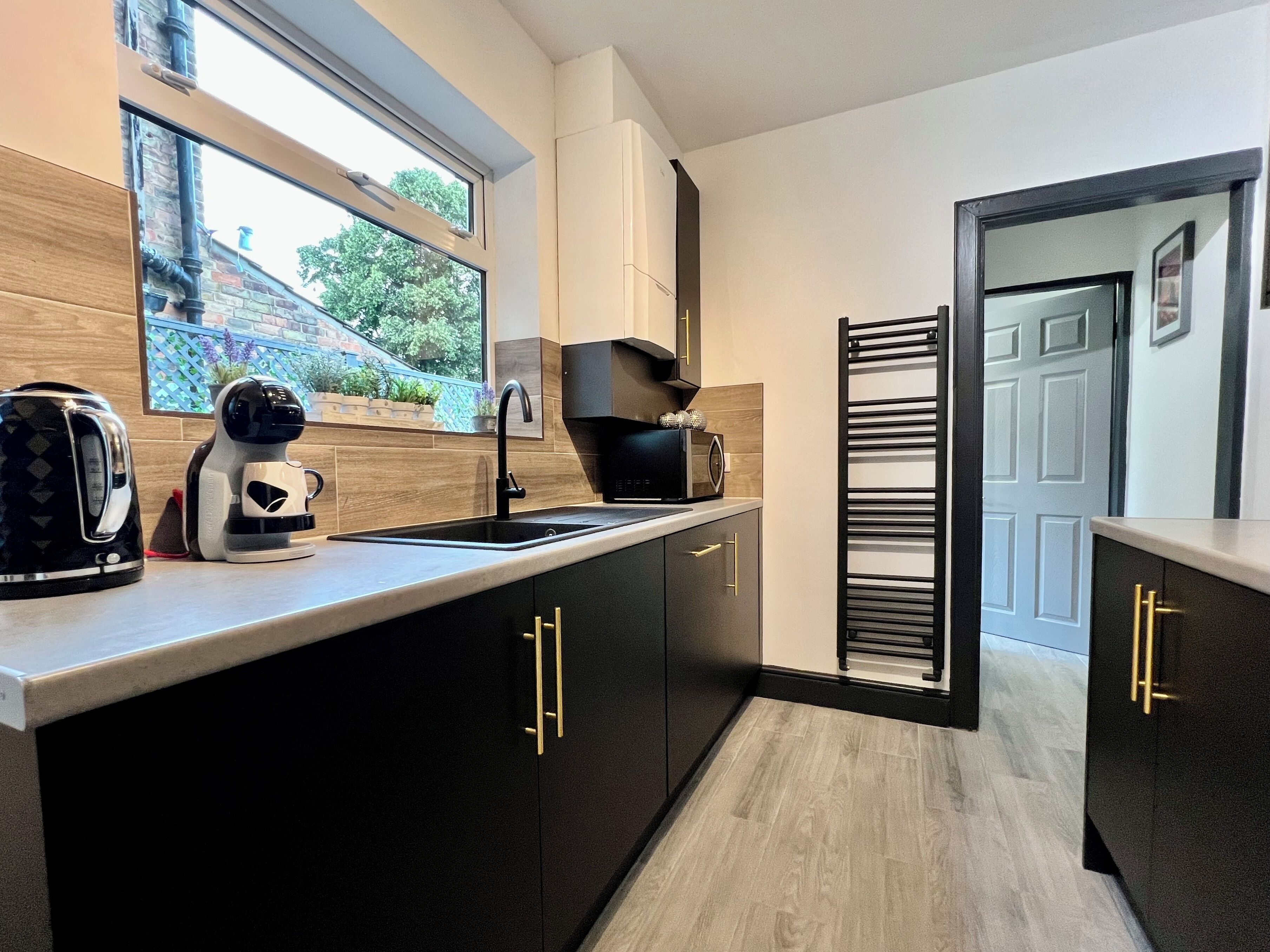 Una cocina moderna con armarios negros, un lavamanos de acero inoxidable y una ventana con vistas a un jardín.
