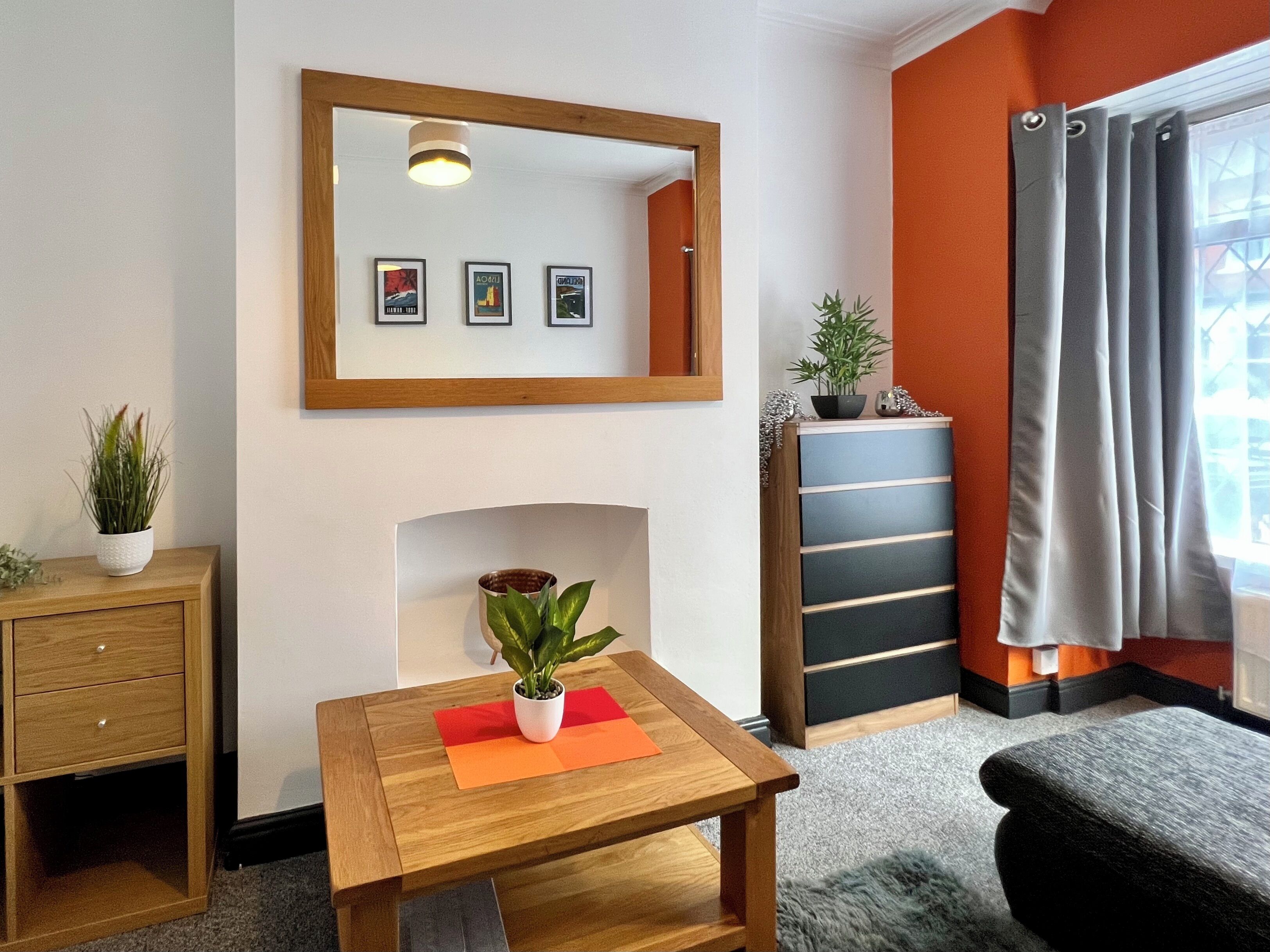 Ein modernes Zimmer mit einem Holztisch, einem Spiegel, gerahmten Bildern, einer Pflanze, einem Schrank und einem Fenster mit Vorhängen.