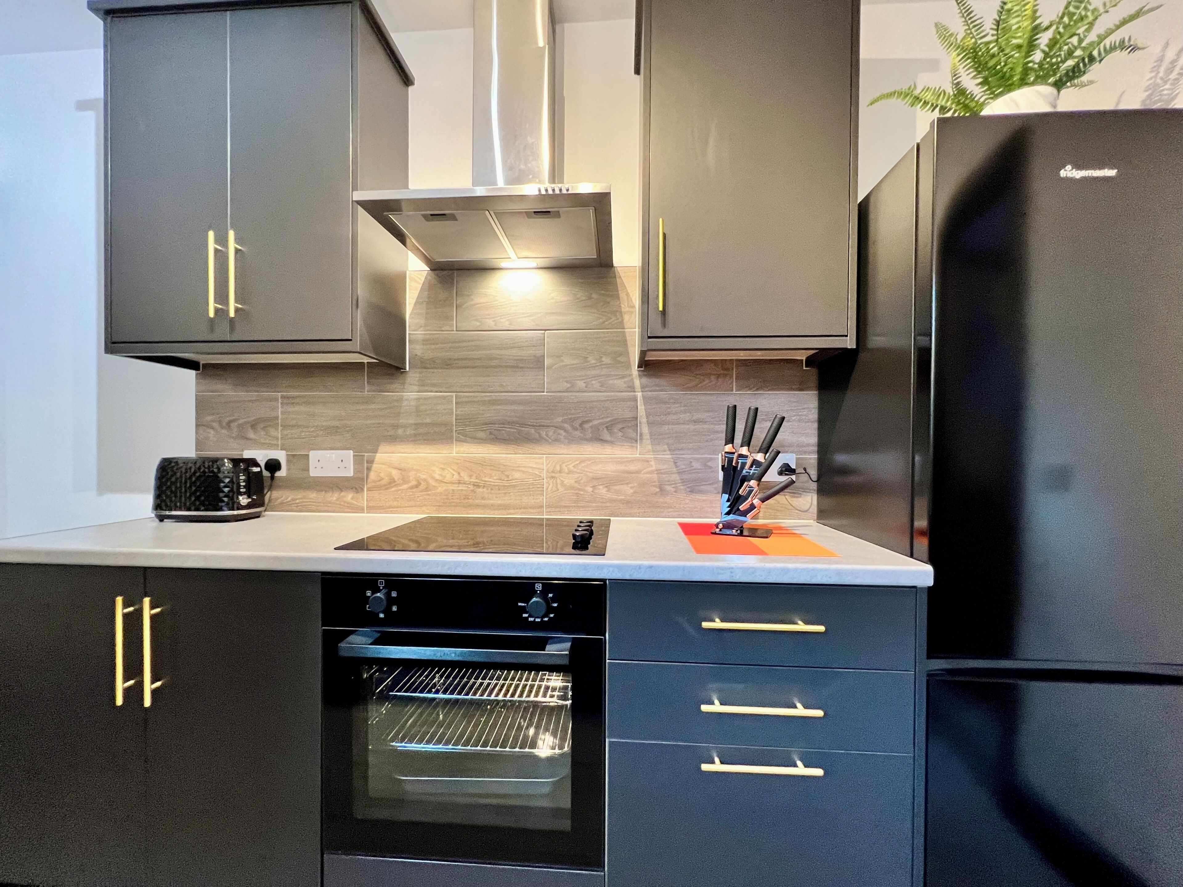 Une cuisine moderne avec des meubles de rangement aux couleurs sombres, un four encastré et un réfrigérateur en acier inoxydable.