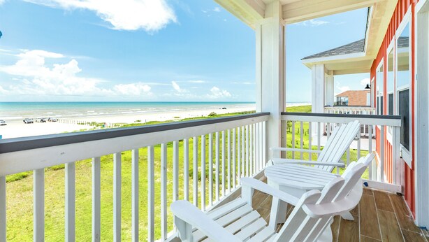 Un balcon avec des fauteuils Adirondack blancs donnant sur une plage.