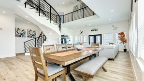 Un vaste espace dédié à la salle à manger, avec une table et des chaises en bois, un escalier et une vue sur la cuisine.