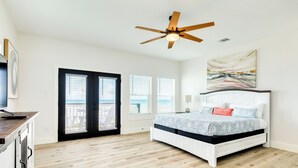 Une chambre avec un lit, un ventilateur de plafond, un tableau et une vue sur l’extérieur, visible à travers la porte.