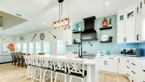 Une cuisine moderne avec des meubles blancs, un îlot central doté de tabourets, une hotte noire et un dosseret de carrelage bleu.