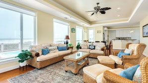 A spacious living room with wicker furniture, a glass coffee table, and large windows offering a view of the ocean. - Beachfront w/POOL ON DECK, Private Dune Walkover, 5 Bedrooms (Galveston)