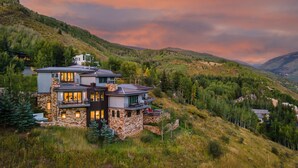 A modern multi-story house with a stone facade, large windows, and a balcony overlooking a mountainous landscape. - Perfect Perch With All the Views | Radiance Retreat (Vail)