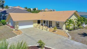 A single-story house with a tiled roof, a front yard with landscaping, and a clear blue sky. - House with Beach Access Point Just Around the Corner! (Marco Island)