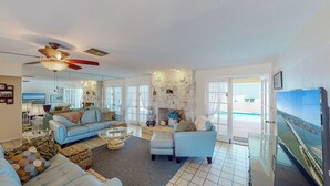 A spacious living room with a stone fireplace, a ceiling fan, and a large TV. - House with Beach Access Point Just Around the Corner! (Marco Island)