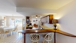 A kitchen with a bar area, white tiled flooring, and a dining area with white chairs. - House with Beach Access Point Just Around the Corner! (Marco Island)