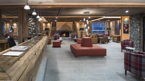 A spacious lobby with a long reception desk, comfortable seating areas, and a stone wall with a fireplace. - Wifi, 50m from ski lifts, fitness, swimming pool, sauna, hammam, balcony, ski locker, 90m², Chamonix (Chamonix-Mont-Blanc)