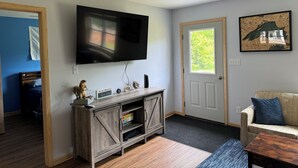 Una sala de estar con un televisor montado en la pared, un mueble de entretenimiento de madera, una puerta con ventanal y un sofá.