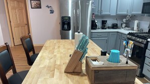 Una cocina con una mesa de madera, sillas, una cafetera, un refrigerador y una estufa.