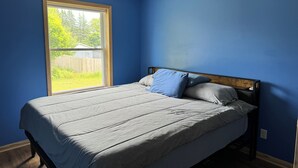 Un dormitorio con un ventanal grande, una cama con ropa de cama gris y paredes azules.