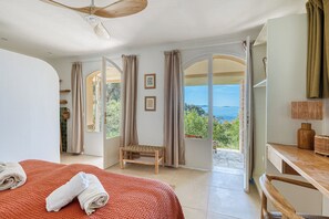 Une chambre avec un lit, une chaise, un bureau et une vue sur la mer.