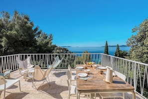 Une terrasse avec une table dressée pour le dîner, offrant une vue panoramique sur la mer et les collines.