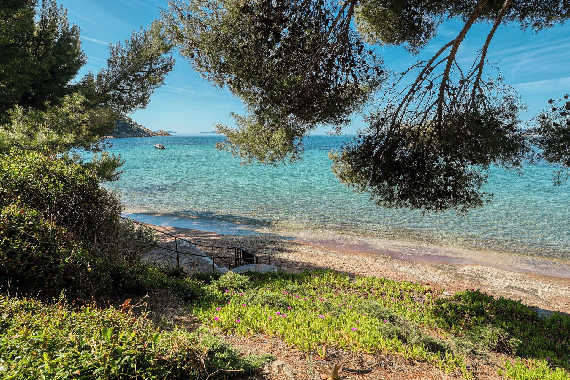 A coastal landscape with clear water, a sandy beach, and surrounding greenery.