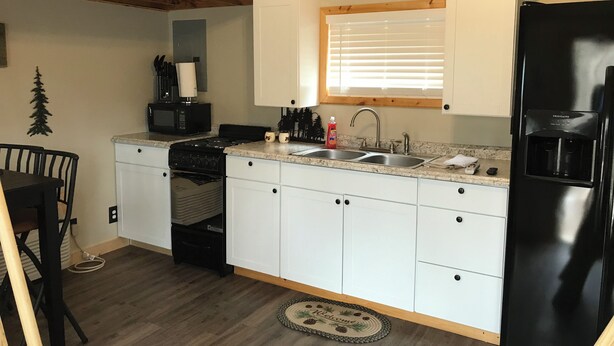 A compact kitchen with white cabinets, a black refrigerator, a microwave, and a stove. - Judy's Place - 1BR, 1 Bath w/ Q, K, and Twin bed. Full kitchen. (Putney)