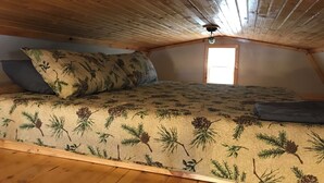 A cozy attic bedroom with a wooden ceiling, a bed with a floral-patterned bedspread, and a window letting in natural light. - Judy's Place - 1BR, 1 Bath w/ Q, K, and Twin bed. Full kitchen. (Putney)
