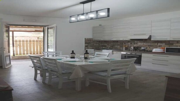 Una cocina moderna con armarios blancos, un comedor con mesa preparada para cuatro comensales, y un puerta corrediza de vidrio que da a un espacio exterior.