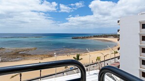 Une vue sur la plage depuis un balcon doté d’une balustrade, avec une plage de sable et un ciel bleu dégagé.
