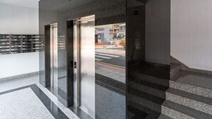 Un ascenseur moderne avec des portes en verre, un sol en marbre et une vue sur la rue.