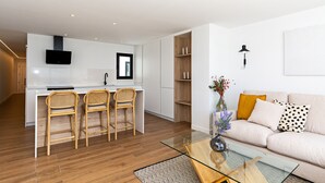 Une cuisine moderne avec des meubles blancs, un îlot central doté de tabourets de bar et un téléviseur à écran plat fixé au-dessus de l’îlot.