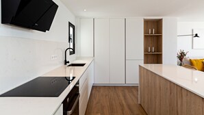 Une cuisine moderne avec des meubles blancs, une plaque de cuisson à induction noire et des étagères en bois.