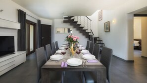 Un comedor moderno con una mesa larga dispuesta para seis comensales, un televisor de pantalla plana a la izquierda y una escalera que conduce a un nivel superior.