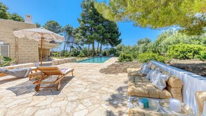 Une terrasse en pierre avec une piscine, des chaises longues et un espace salon abrité.