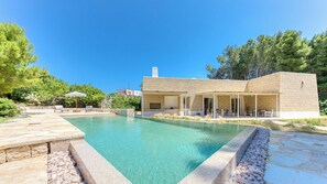 A modern house with a swimming pool, outdoor seating, and a stone facade.