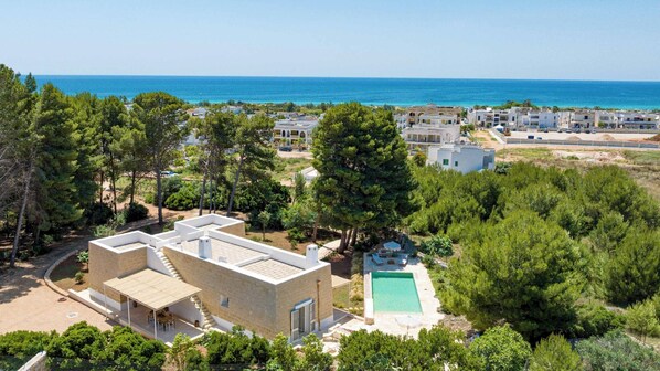 A modern building with a pool, surrounded by trees and a view of the sea.