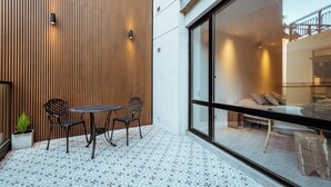Un patio exterior moderno con un muro de listones de madera, un ventanal de vidrio que da al interior y un piso de baldosas.