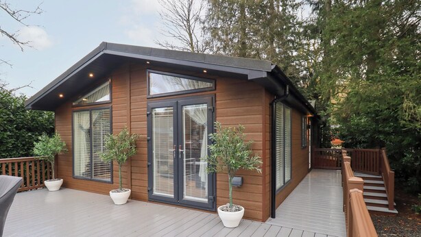 A modern wooden cabin with large windows, a deck, and potted plants. - Unique Luxury Lodge (Windermere)