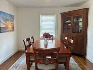 Een eetkamer met een houten tafel en stoelen, een kast met glazen deuren en een raam met zonwering.