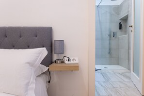 A bedroom with a bed, a bedside table with a lamp, and a power strip. Adjacent to the bedroom is a glass-enclosed shower area with a showerhead and a toilet. - APT Rome 5 BDRM’s (Roma)