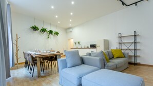 A modern living room with a dining area, a grey sofa, and a wooden dining table set for four. - APT Rome 5 BDRM’s (Roma)