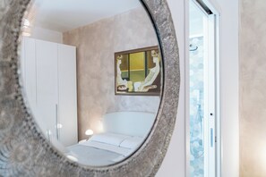 Ein Schlafzimmer mit Bett, Nachttisch, einem Gemälde und einem Badezimmer mit Dusche.