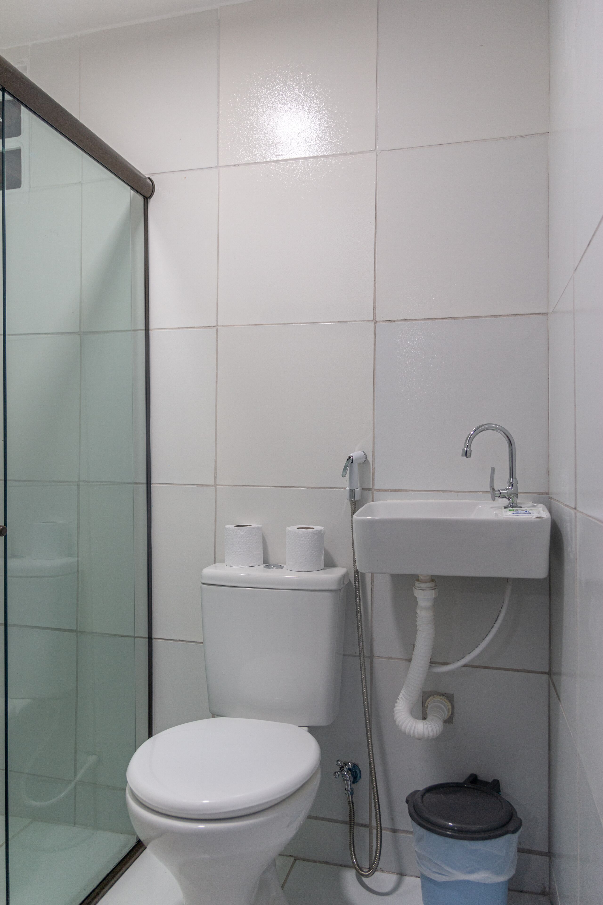 Ein Badezimmer mit Toilette, einer Duschkabine aus Glas und einem Waschbecken mit Brausekopf.