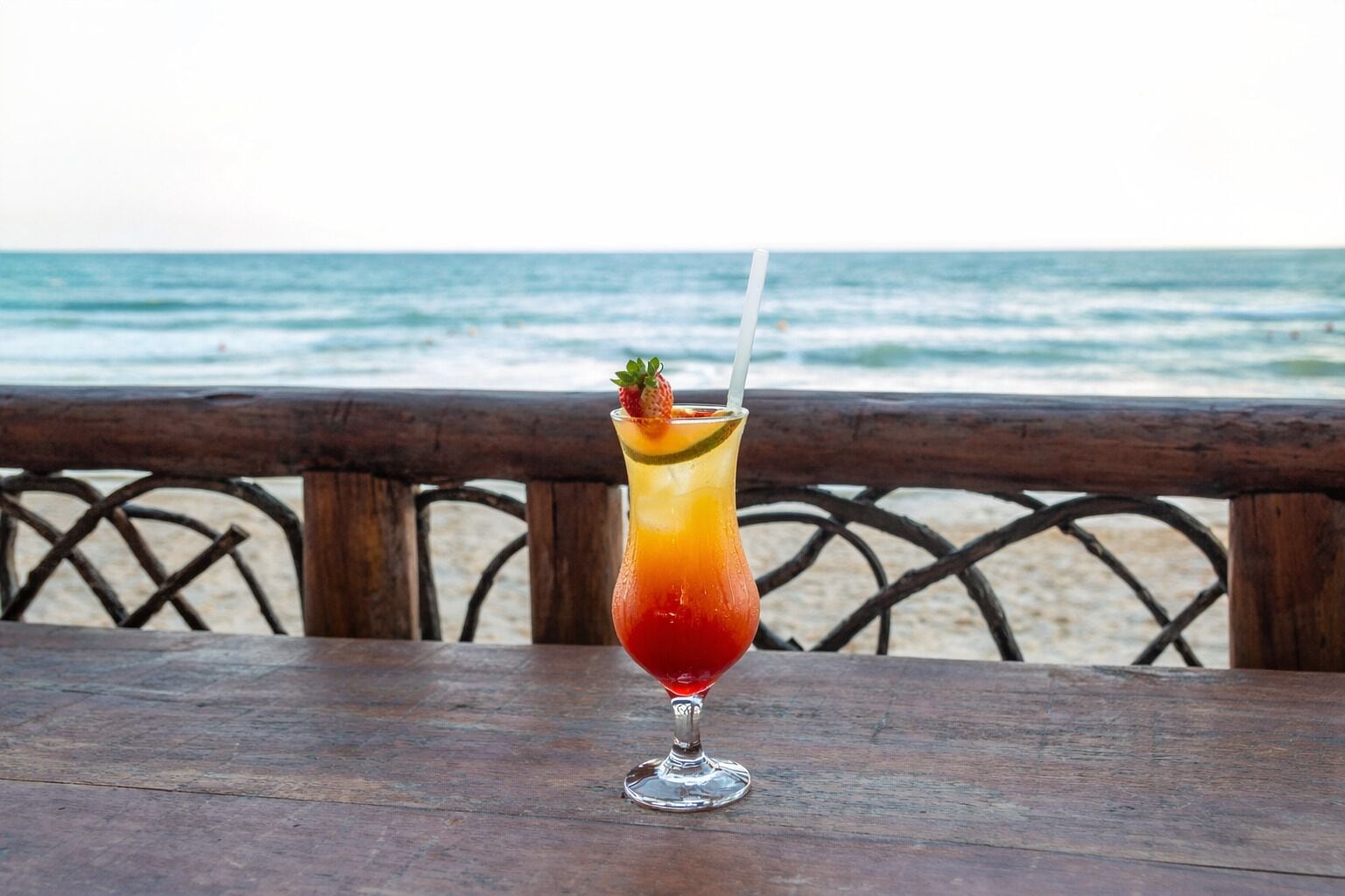 A cocktail on a wooden table with a view of the ocean.